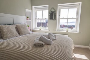 A bedroom with a bed, two windows, a mirror, and a view of a marina. - Set in Scarborough’s historic old town, Sandgate Seaview is a charming property with over 300 years of character. Beautifully furnished throughout, it offers stunning views across the sea and coastline for a memorable stay. (Scarborough)
