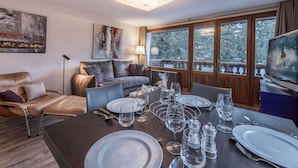 Un comedor con una mesa dispuesta para cuatro personas, un sofá, una silla y un televisor.