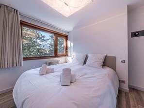 Ein Schlafzimmer mit einem großen Bett, einem Fenster mit Vorhängen, einem Heizkörper und einem Dachfenster.