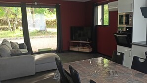 Ein kompakter Wohnbereich mit Sofa, Esstisch, Küchenzeile inklusive Mikrowelle und Backofen sowie einem Fernseher.