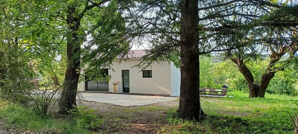 Une maison entourée d’arbres, avec une allée en gravier et un banc au fond.