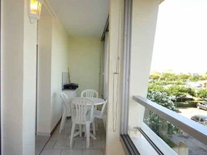A balcony with a table and chairs, a view of the street, and a building in the background. - Apartment with parking, mountain view - 4 guests (Le Barcarès)