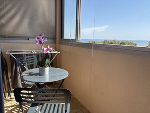 Ein Balkon mit Tisch und Stühlen, einer Topfpflanze und Blick auf das Meer.