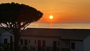 A coastal scene with a sunset, a tree, and a building with a tiled roof. - Apartment with sea view, parking - 4 guests (Fleury-Saint-Pierre-la-Mer)