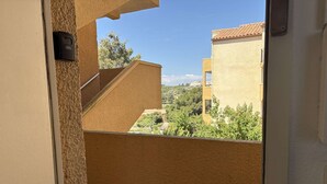 Udsigt fra en balkon med klar himmel, en bygning med et tagtækket tag og et fjerntliggende landskab.