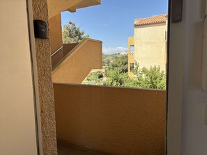 Blick von einem Balkon mit blauem Himmel, einem Gebäude mit Ziegeldach und einer entfernten Landschaft.