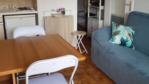 Un ambiente compatto con angolo cottura, zona pranzo e divano con cuscino a motivi floreali.
