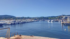 Una marina con imbarcazioni ormeggiate, cielo sereno e un paesaggio collinare sullo sfondo.