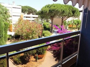 Ein Balkon mit Blick auf einen Garten, einen Baum und ein Gebäude im Hintergrund.