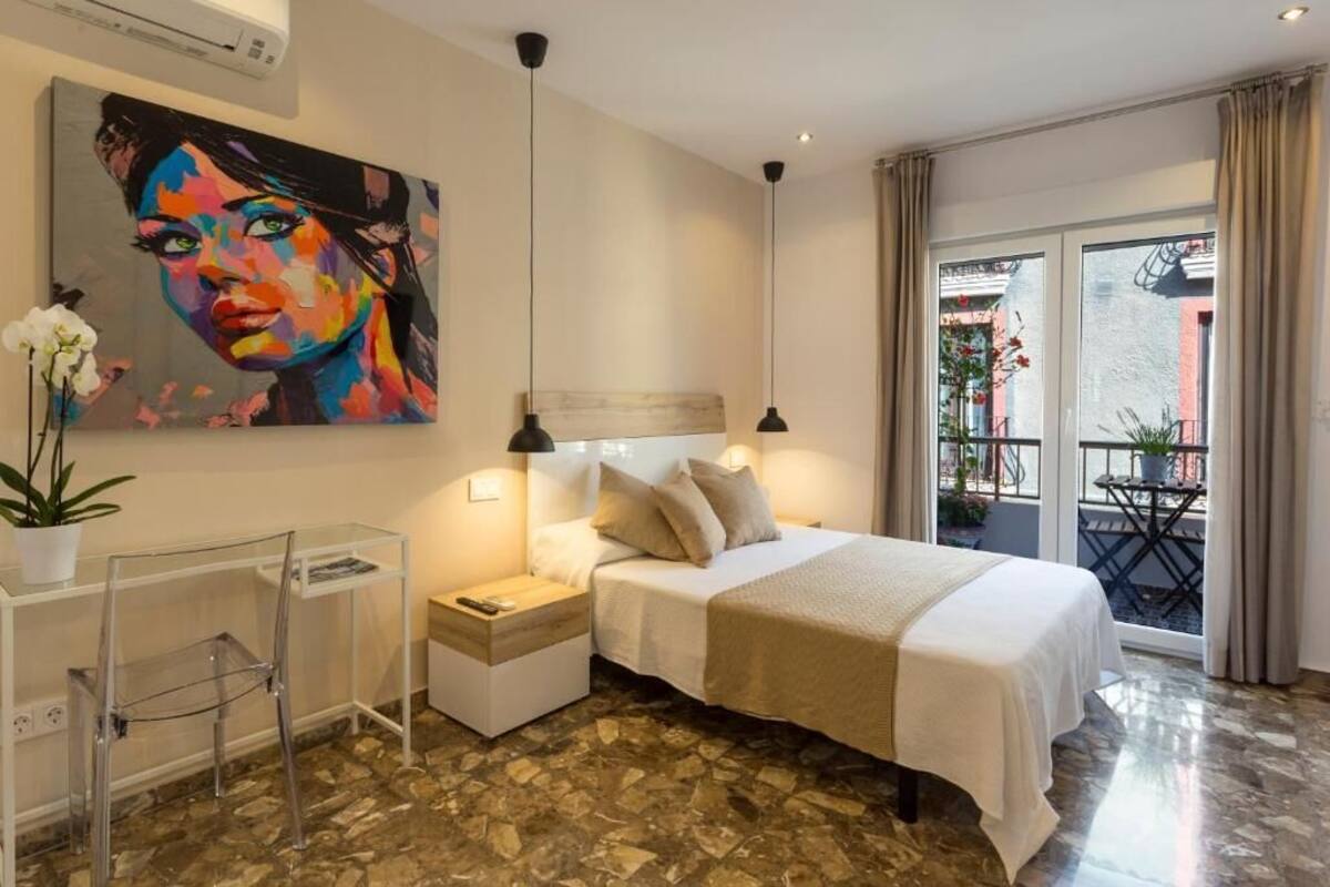 Habitación de hotel con cama, mesitas de noche, un cuadro, planta en maceta y vistas al exterior.