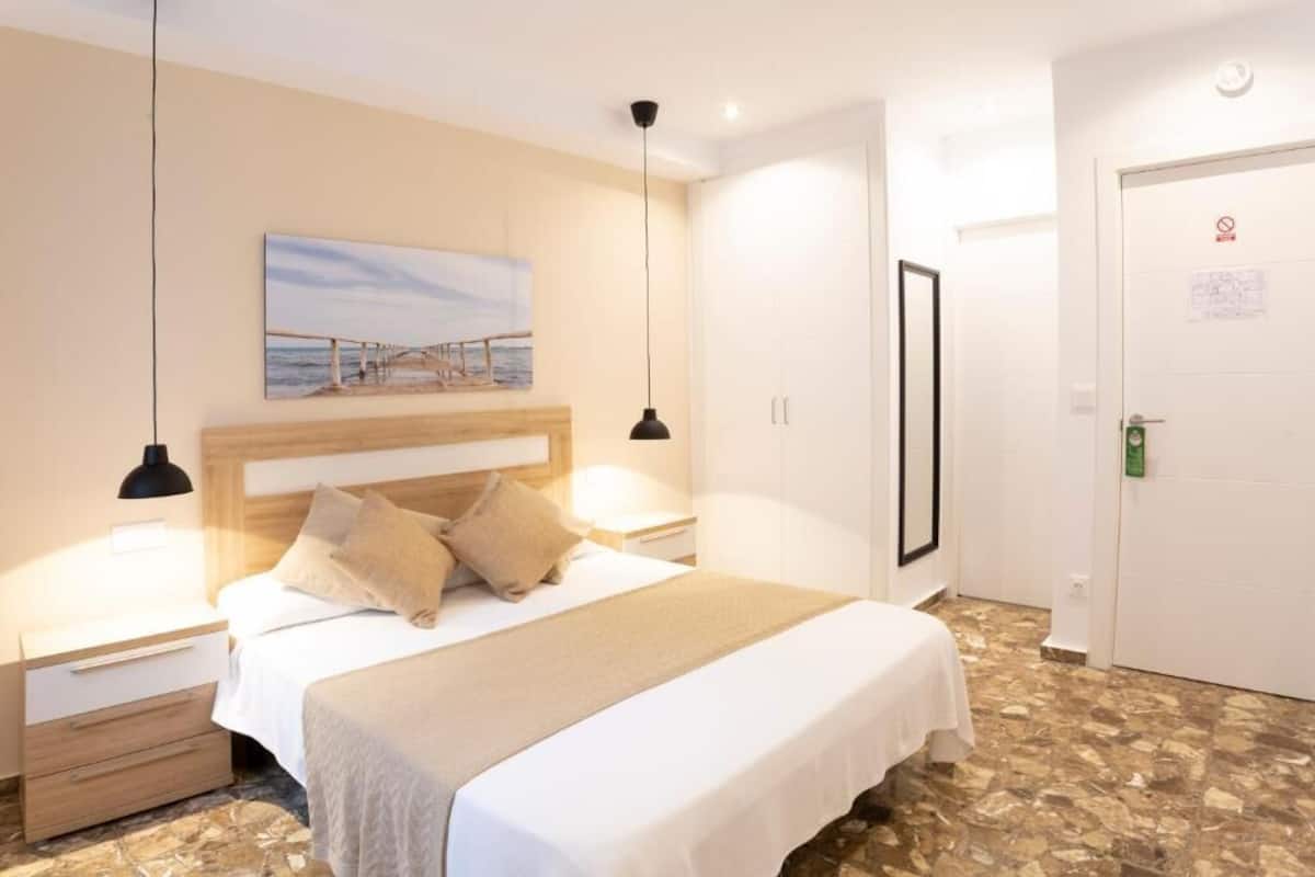 Un dormitorio con cama, mesitas de noche, un cuadro, una puerta con un cartel y un suelo estampado.