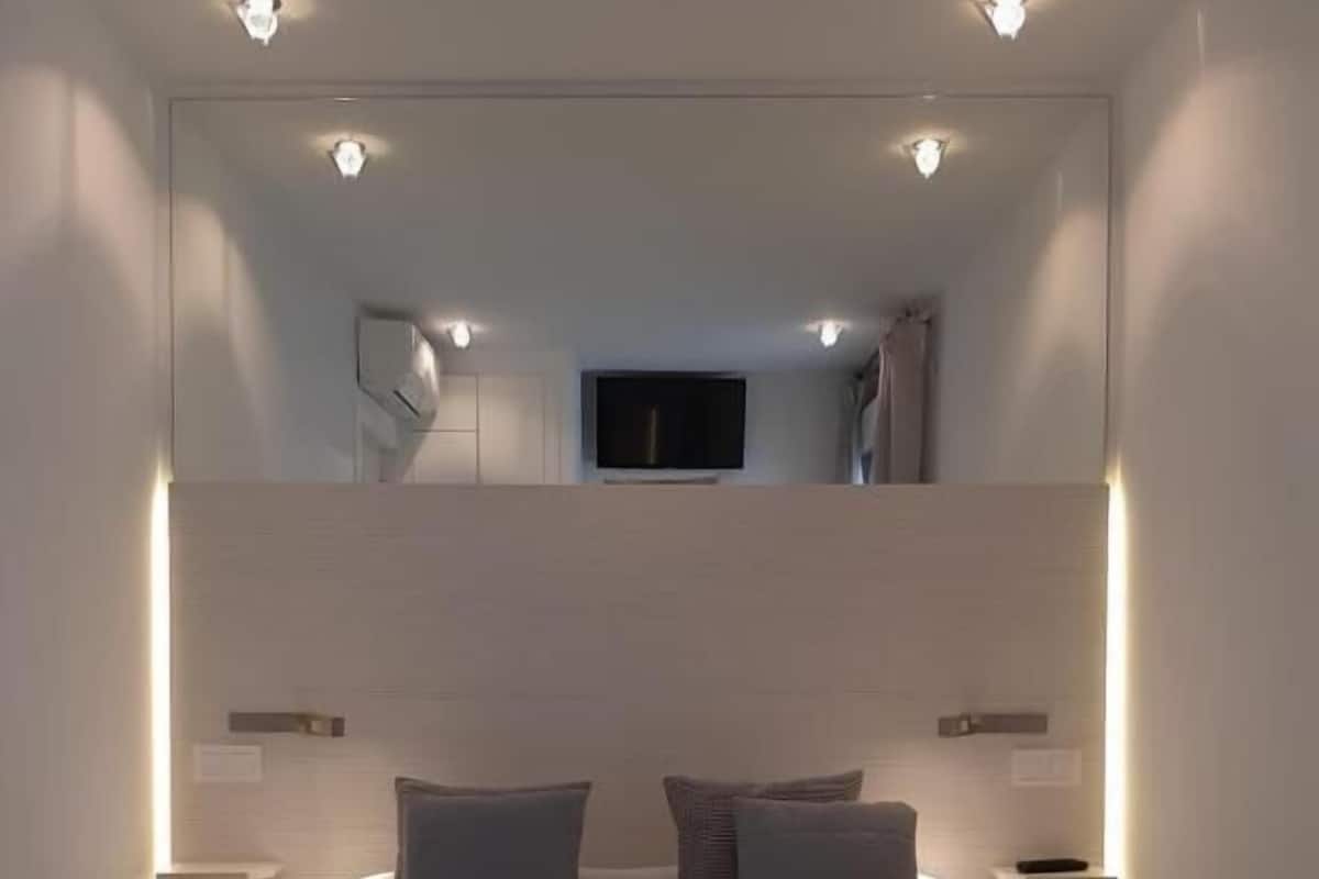 Un dormitorio moderno con una cama grande, mesitas de noche, un televisor y un espejo.