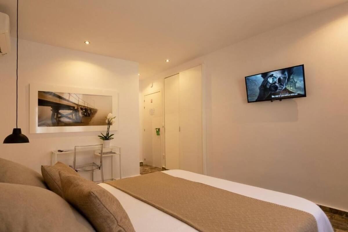 Habitación de hotel con cama, televisión en la pared, escritorio con silla e imagen enmarco.