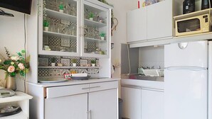 Een keuken met witte kastjes, een magnetron en een koelkast. Er staan decoratieve items op de planken en een vaas met bloemen op het aanrecht.