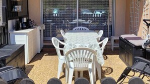 Een terras met een tafel, stoelen, een witte kast en een schuifdeur.