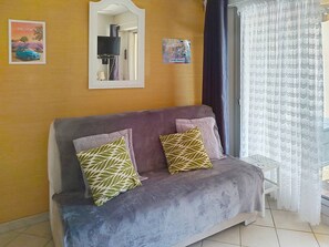A room with a purple sofa, two patterned cushions, a mirror, a poster of Provence, and a sign for Saint-Tropez. - Studio with terrace, pool, and parking (Bormes-les-Mimosas)