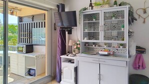 Een keuken met een televisie, kastjes en een balkon.