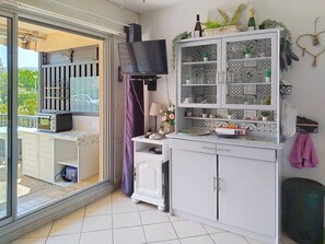A kitchen with a TV, cabinets, and a balcony. - Studio with terrace, pool, and parking (Bormes-les-Mimosas)