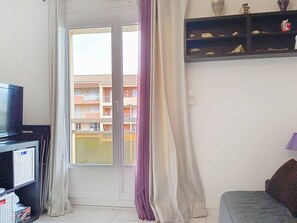 Ein Zimmer mit Fernseher, einer Couch, einem Fenster mit Vorhängen und einem Regal mit Dekoration.