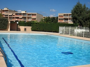 A swimming pool with clear blue water, surrounded by a fence and a building with multiple balconies. - Bright studio with 15m² terrace, parking, La Favière (Bormes-les-Mimosas)