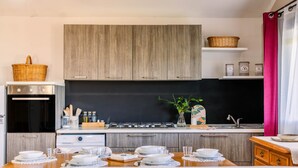 Une cuisine moderne avec des meubles en bois, une cuisinière à gaz et un coin repas agrémenté d’assiettes et de verres blancs.