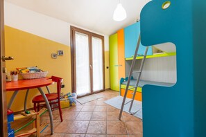 Une pièce avec une table rouge, une chaise rouge, un lit superposé, une échelle et une porte avec une fenêtre.