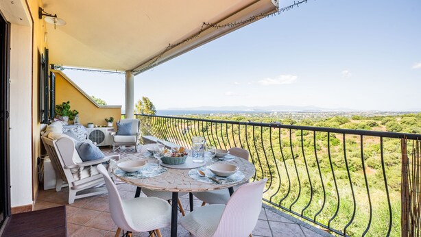 Un balcon avec une table dressée pour le dîner, des chaises et une vue sur un paysage verdoyant.