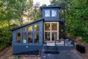 Eine moderne Hütte mit großen Fenstern, einer Holzterrasse und einer Steinfassade.
