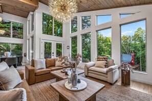 Ein geräumiges Wohnzimmer mit großen Fenstern, einer Holzbalkendecke und einer modernen Kronleuchter.