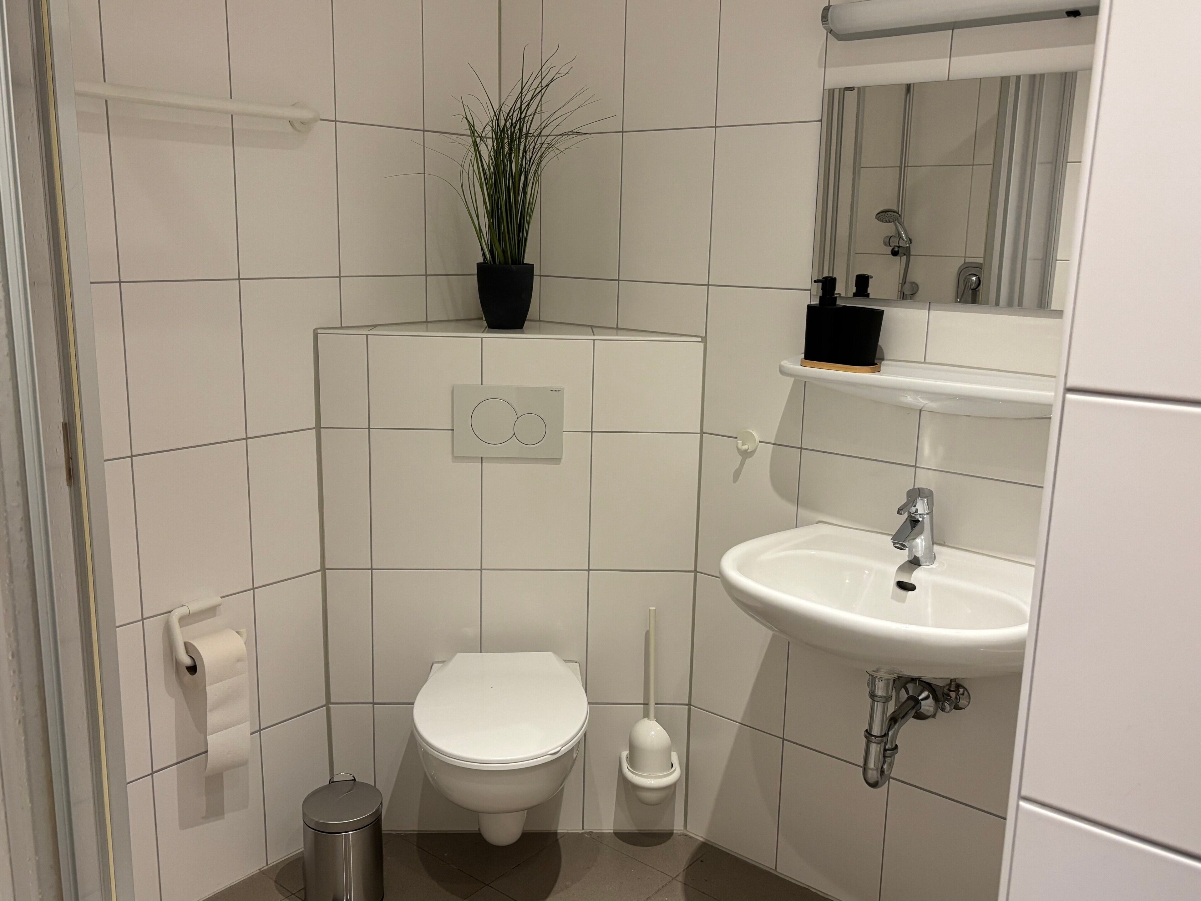 Een badkamer met toilet, bidet, wastafel, spiegel en een potplant.