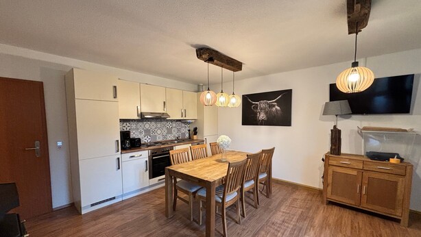 A modern kitchen with white cabinets, a wooden dining table, and pendant lights.