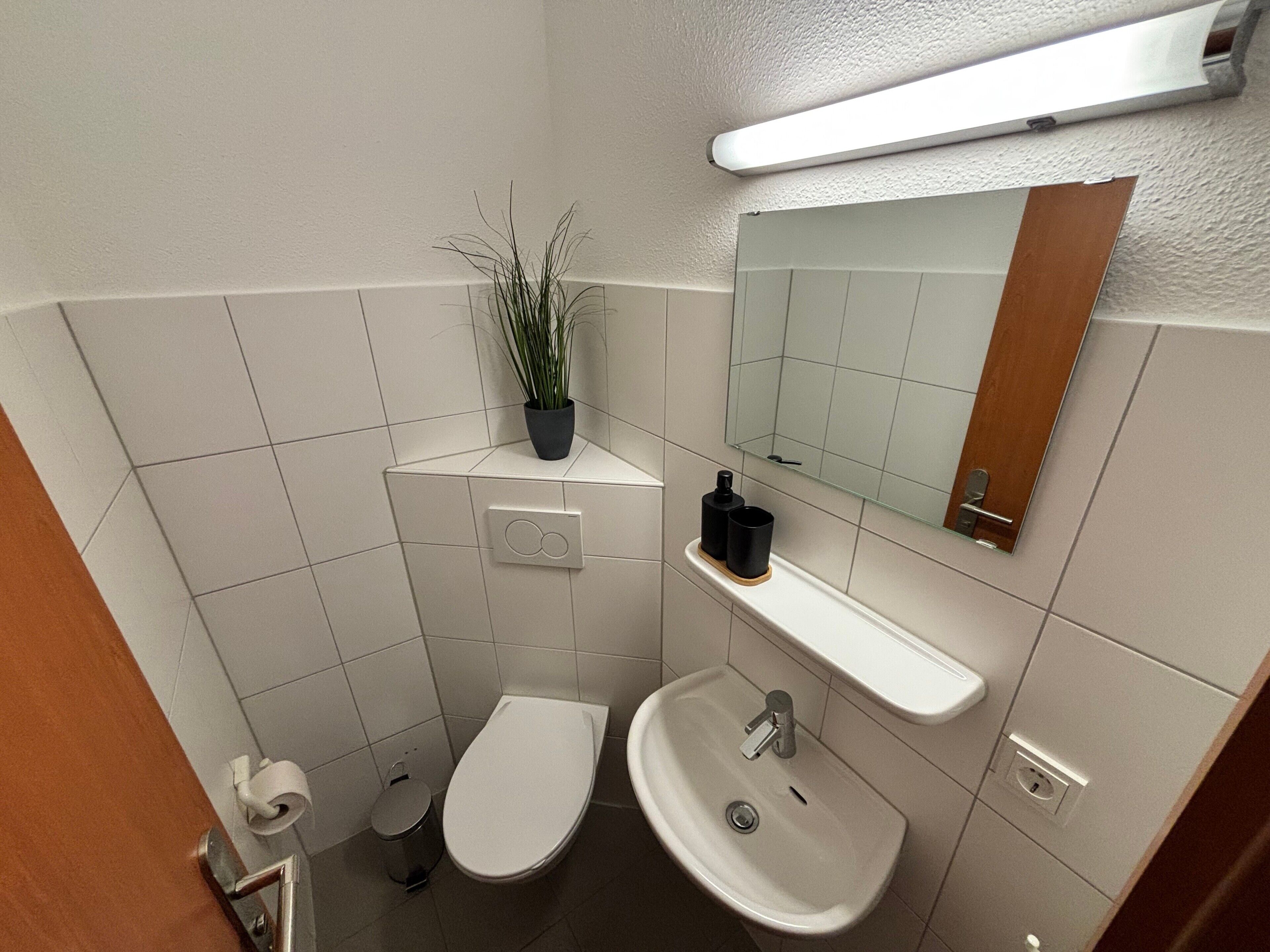 Een badkamer met toilet, bidet, wastafel, spiegel en een potplant.