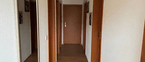 Un pasillo con suelo de madera, paredes blancas y puertas de madera.