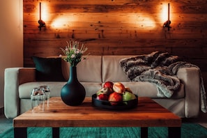 A cozy living room with a wooden coffee table, a vase with flowers, a bowl of fruit, and a sofa with a fur throw. - Forestum - Black Forest Luxury Apartments - Apartment Auerhahn with sauna (Sankt Blasien)