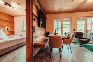 A modern interior with a wooden ceiling, a bed with white linens, a dining area with chairs, and large windows offering a view of greenery. - Forestum - Black Forest Luxury Apartments - Apartment Auerhahn with sauna (Sankt Blasien)
