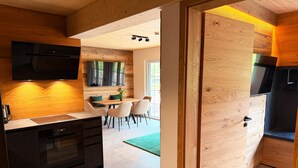Eine moderne Küche mit Holzelementen, ein Essbereich mit einem grünen Teppich und ein an der Wand befestigter Fernseher.