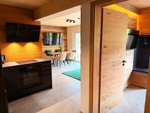 Eine moderne Küche mit Holzelementen, ein Essbereich mit einem grünen Teppich und ein an der Wand befestigter Fernseher.