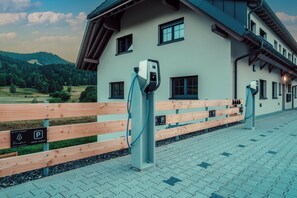 A building with a parking area, electric vehicle charging stations, and a wooden fence. - Forestum - Black Forest Luxury Apartments - Apartment Auerhahn with sauna (Sankt Blasien)