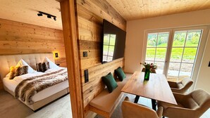 Ein gemütliches Zimmer mit einer Couch, einer Holzbank, einem Esstisch mit Stühlen und einem an der Wand montierten Fernseher.