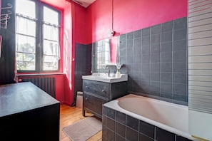A bathroom with a bathtub, a vanity with a mirror, and a window with curtains.