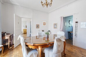 A dining room with a round table, chairs, a chandelier, and framed pictures on the walls.