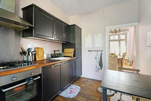 Una cuina amb armaris foscos, un taulell de fusta, una cuina i una finestra amb cortines.