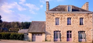 A stone building with multiple windows and a door, surrounded by trees and a clear sky.