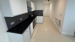 A modern kitchen with white cabinets, black countertops, and a tiled floor. - Radstock Road - Room 2 (Southampton)