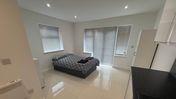 A bedroom with a bed, two windows with blinds, a white radiator, and a black countertop. - Radstock Road - Room 2 (Southampton)