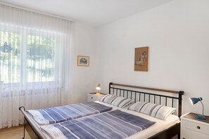 Ein Schlafzimmer mit einem Bett, Nachttischen, einem Fenster mit Vorhängen und Wandbildern.