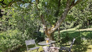 Een tafel met stoelen buiten, met een boom en groen op de achtergrond.