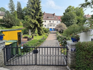 A gated entrance with a paved pathway leading to a building with a red-tiled roof.
