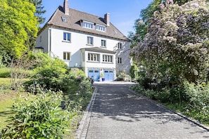 A two-story house with a paved driveway leading to a blue door.