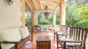 A covered patio with wooden furniture, a white cushioned bench, and a small table. - Villa 'Herdain' with Mountain Views, Wi-Fi, and Air Conditioning (Mal Pas-Bon Aire)
